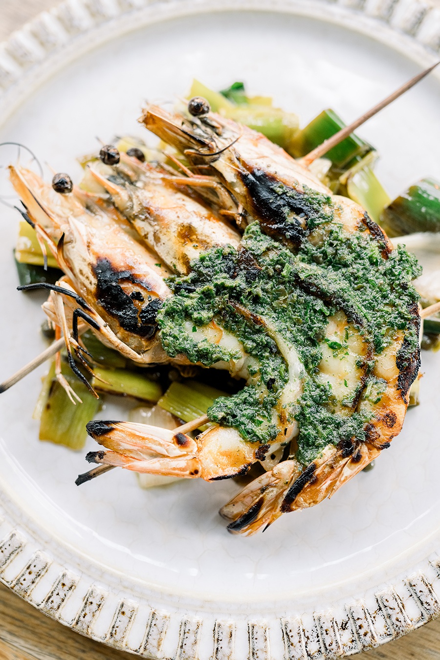 Charred whole shrimp are skewered and garnished with a bright green pesto.