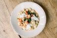 Overhead view of a plate of gnocchi with lobster on a light wooden table.