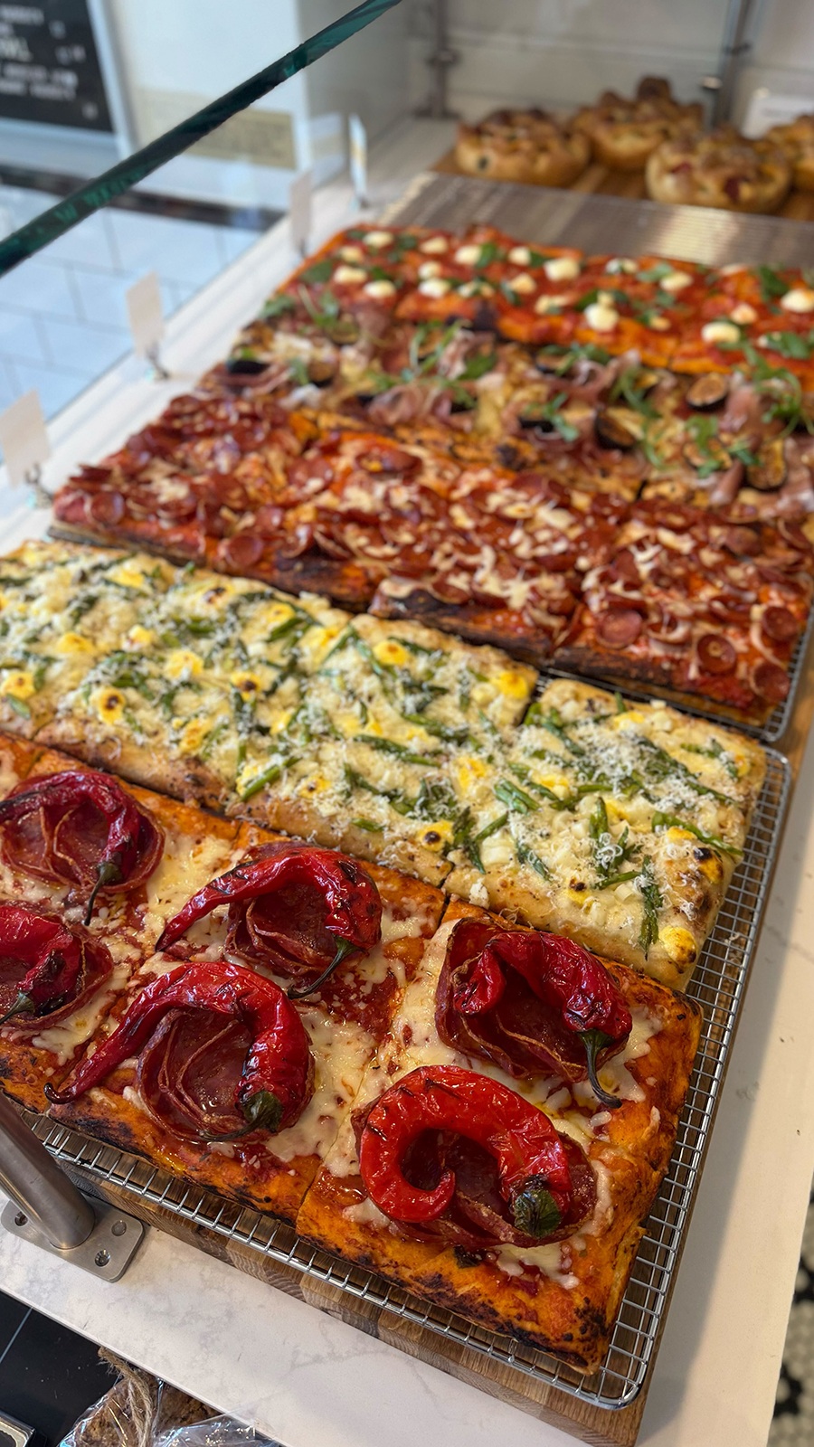 Rectangular pizzas are lined up on a restaurant counter.