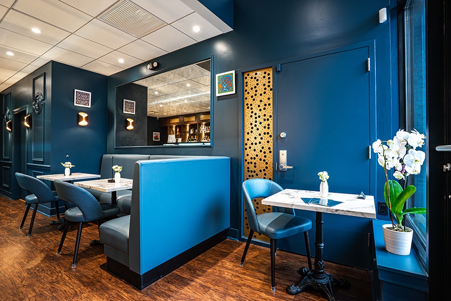 A small restaurant features royal blue walls and chairs with small white marble tables.