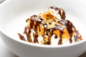 Ice cream-stuffed profiteroles are topped with chocolate sauce, powdered sugar, and slivered nuts.