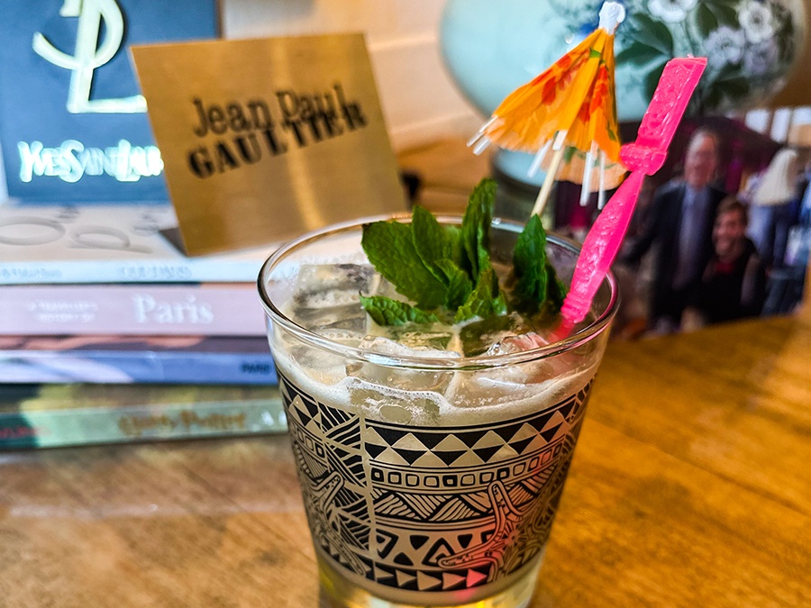 A tropical drink is garnished with fresh mint and a cocktail umbrella, sitting in front of a stack of books.