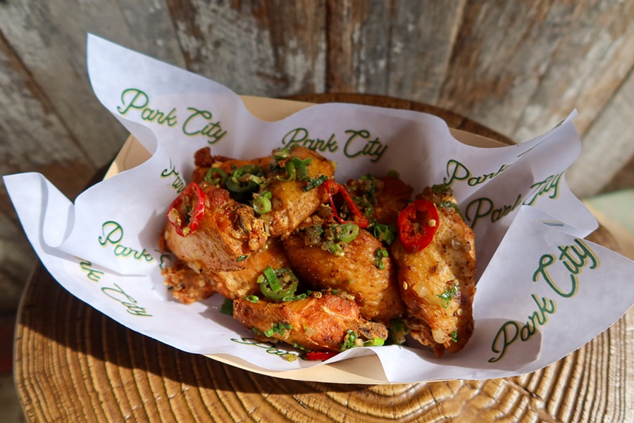 Wings covered with slices of hot pepper sit in a basket on paper with Park City written all over it.