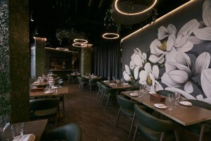 An empty restaurant dining room features dark green and gray tones and a large mural of white flowers.