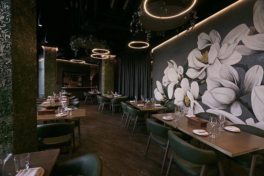 An empty restaurant dining room features dark green and gray tones and a large mural of white flowers.