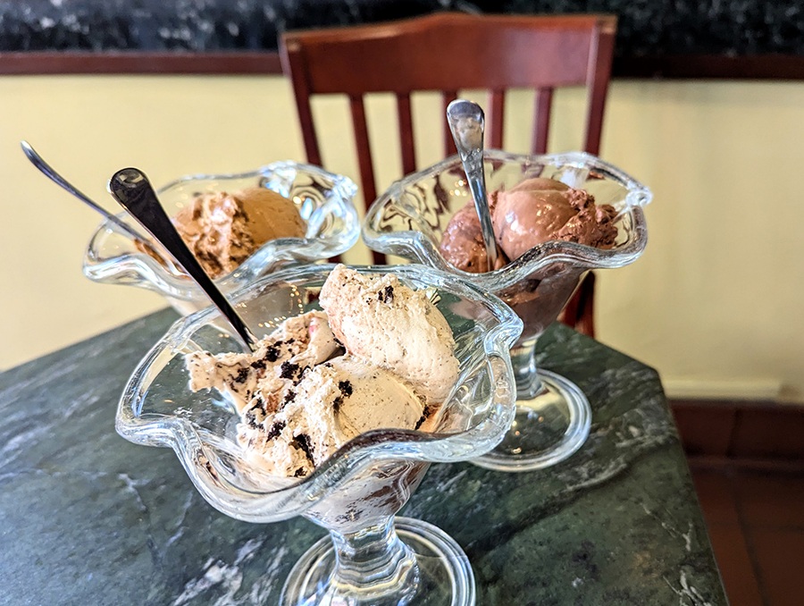 Three different gelato flavors in glass stemmed bowls on a restaurant table.