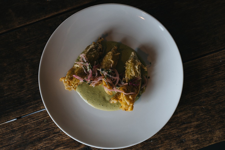 Overhead view of three squash blossoms on a foamy light green puree.