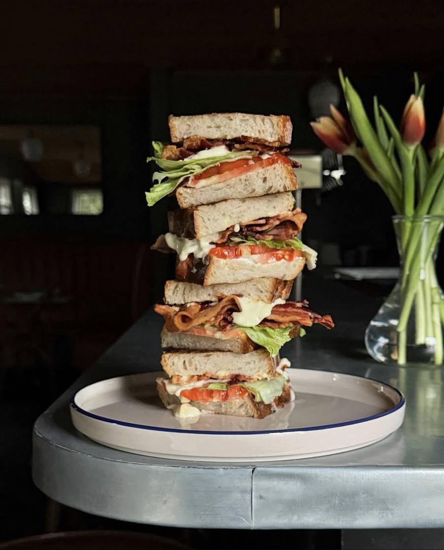 Four thick pieces of a BLT sandwich are stacked high on a plate on the end of a restaurant counter.
