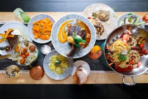 Overhead view of a pork chop, lobster and spaghetti, and other dishes on a restaurant table.