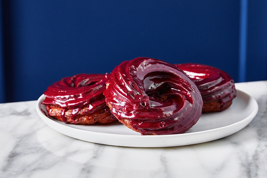 Three crullers sit on a white plate, covered in a deep reddish-blue glaze.