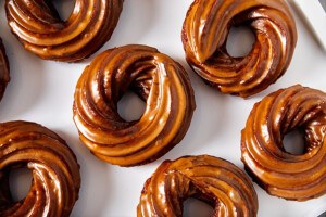 Overhead view of crullers lined up on a white surface, each with a light brown glaze.