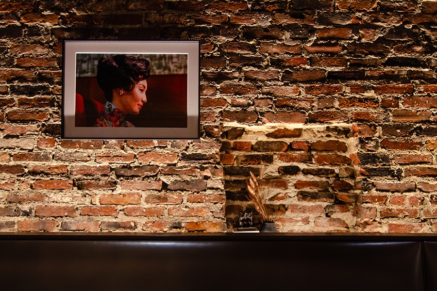 A framed photograph of a woman is displayed on an exposed brick wall over a dark brown banquette.