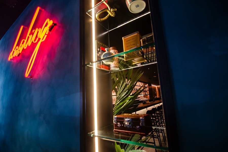 Red neon signage on a teal wall reads "Darling," next to shelves with decorative items in a window that peeks through into a bar.