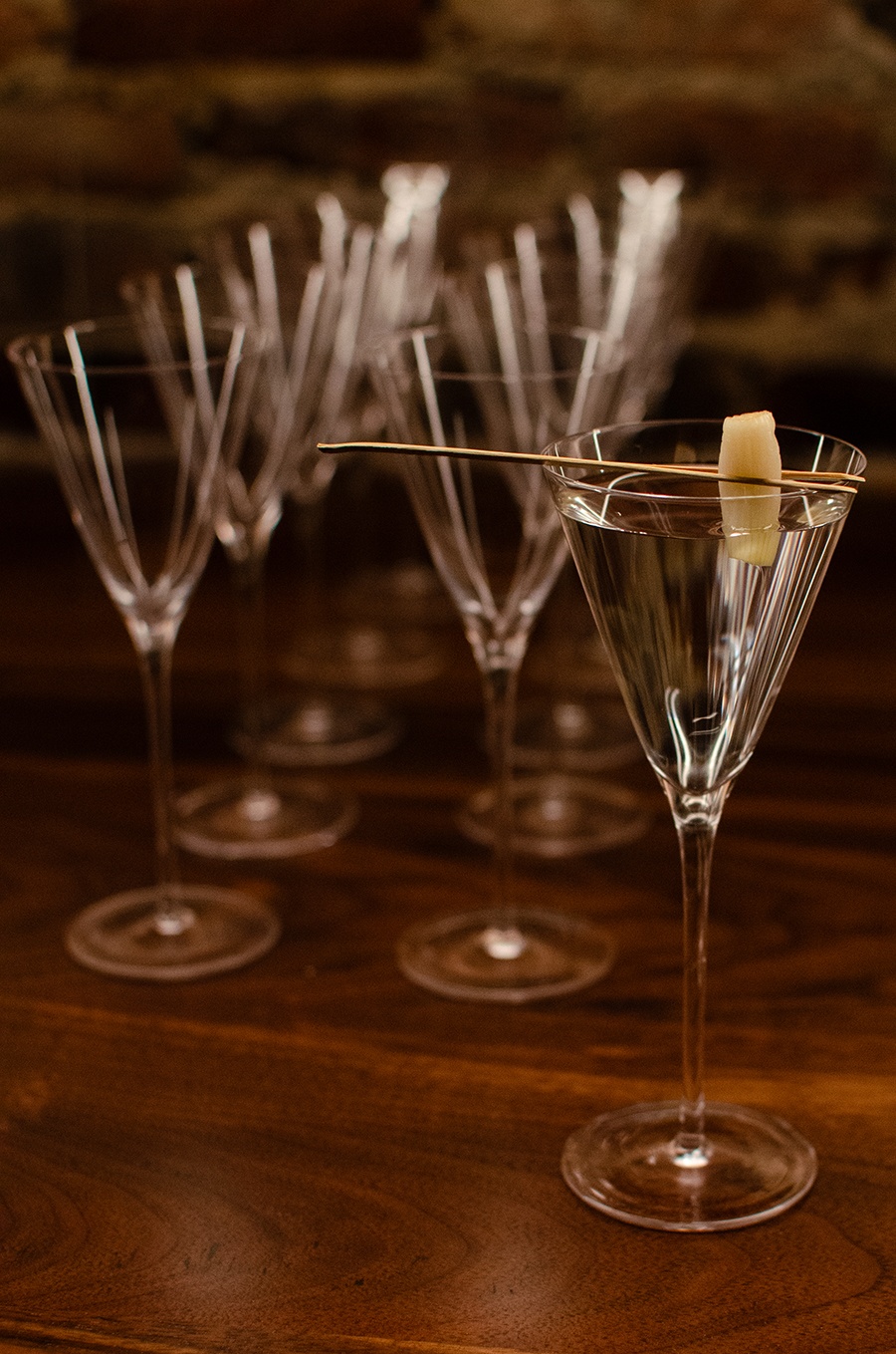 A clear cocktail garnished with a bit of pickled scallion is served in a narrow, small martini-like glass.