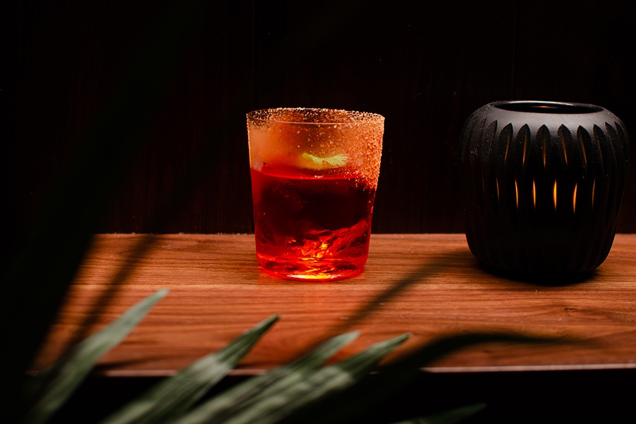 A red cocktail with salt rim sits on a wooden counter next to a black ceramic candleholder.