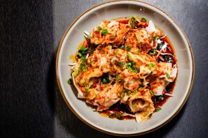 Overhead view of a plate of wontons in a bright red sauce with scallions and crispy onion.