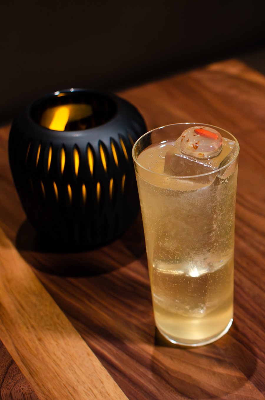 A pale yellow cocktail served in a tall glass is garnished with a circle of clear jelly with tiny flowers inside.