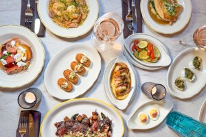 Overhead shot of a plate of food, including croquettes, baked oysters, hanger steak, shrimp and grits, and more.