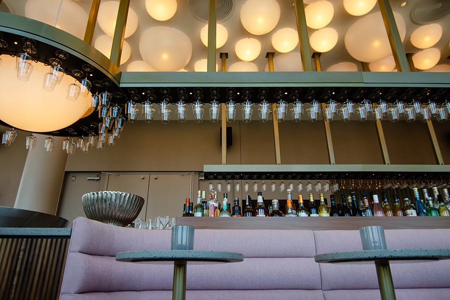 A bar features light pink banquettes and bubble-like light fixtures on the ceiling