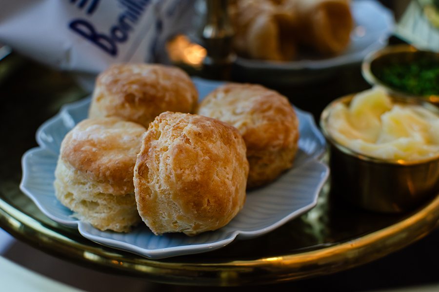 Mini biscuits sit on a gold-rimmed tray with butter, a bag of chips, and more.