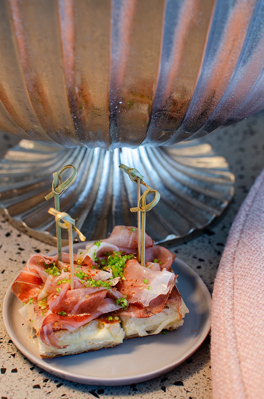 Bite-sized sandwiches with melted cheese and speck, each with a toothpick through it.