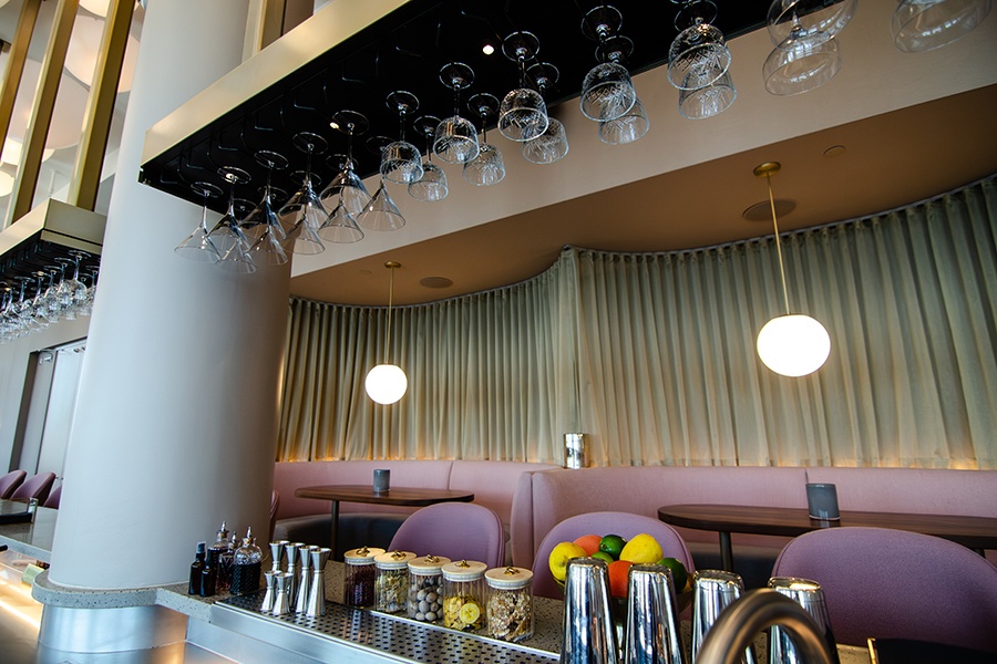 Interior of a bar with u-shaped pale pink booths with beige curtains hanging behind.